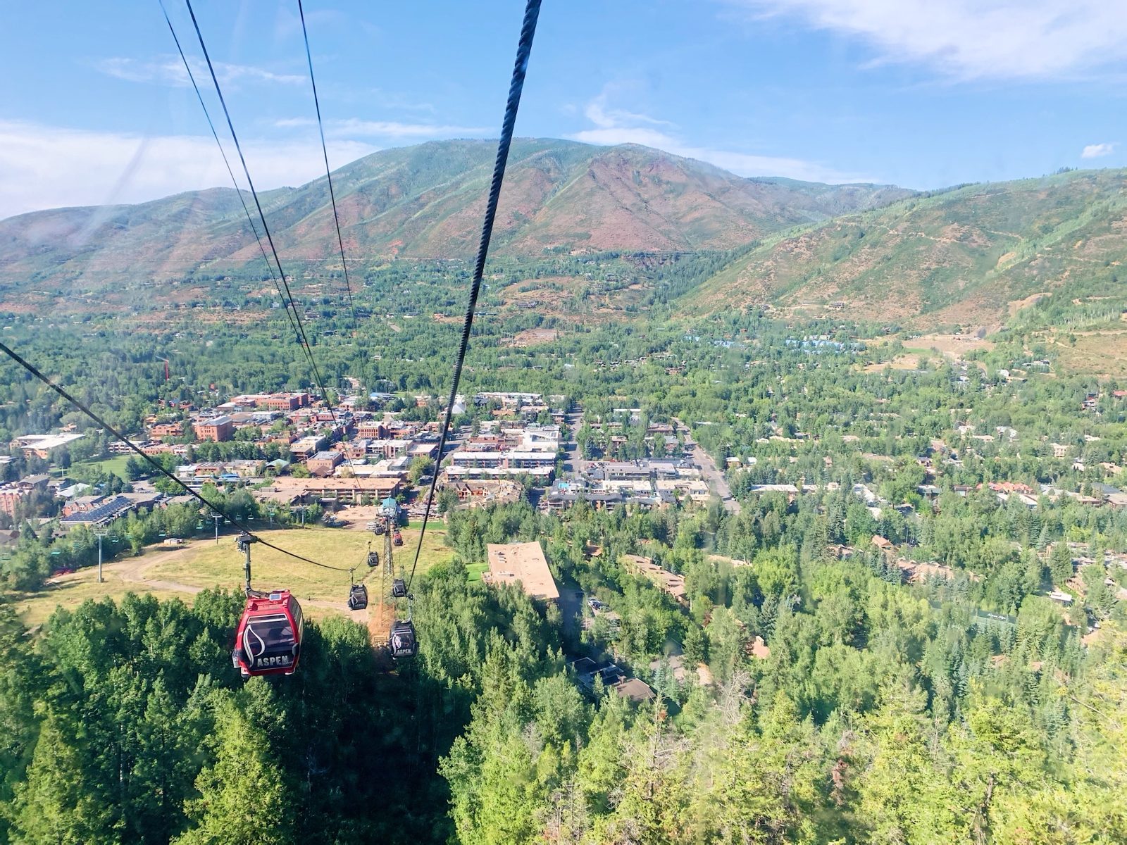 Looking down the Aspen Mountain gondola line over green slopes to the town and valley in summer