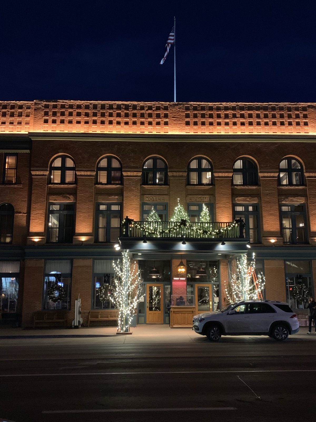 The brick front of the Hotel Jerome lit up at night, with holiday lights and trees on the balcony