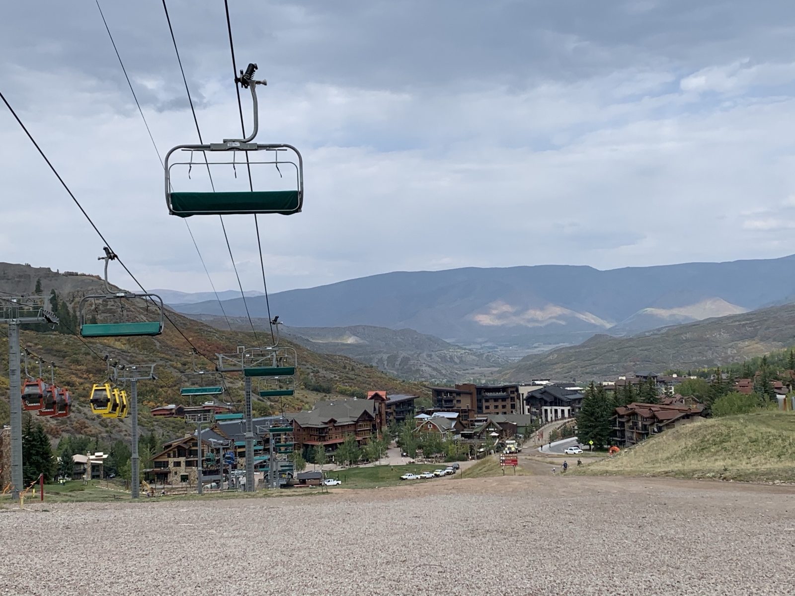 Empty chairlifts and gondola cabins running down to Snowmass Village, with the valley and mountains beyond