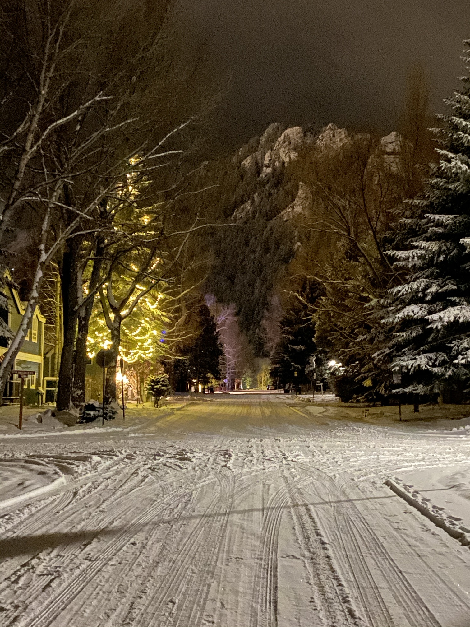 A snowy street on the west side of Aspen at night, trees strung with lights and Shadow Mountain beyond