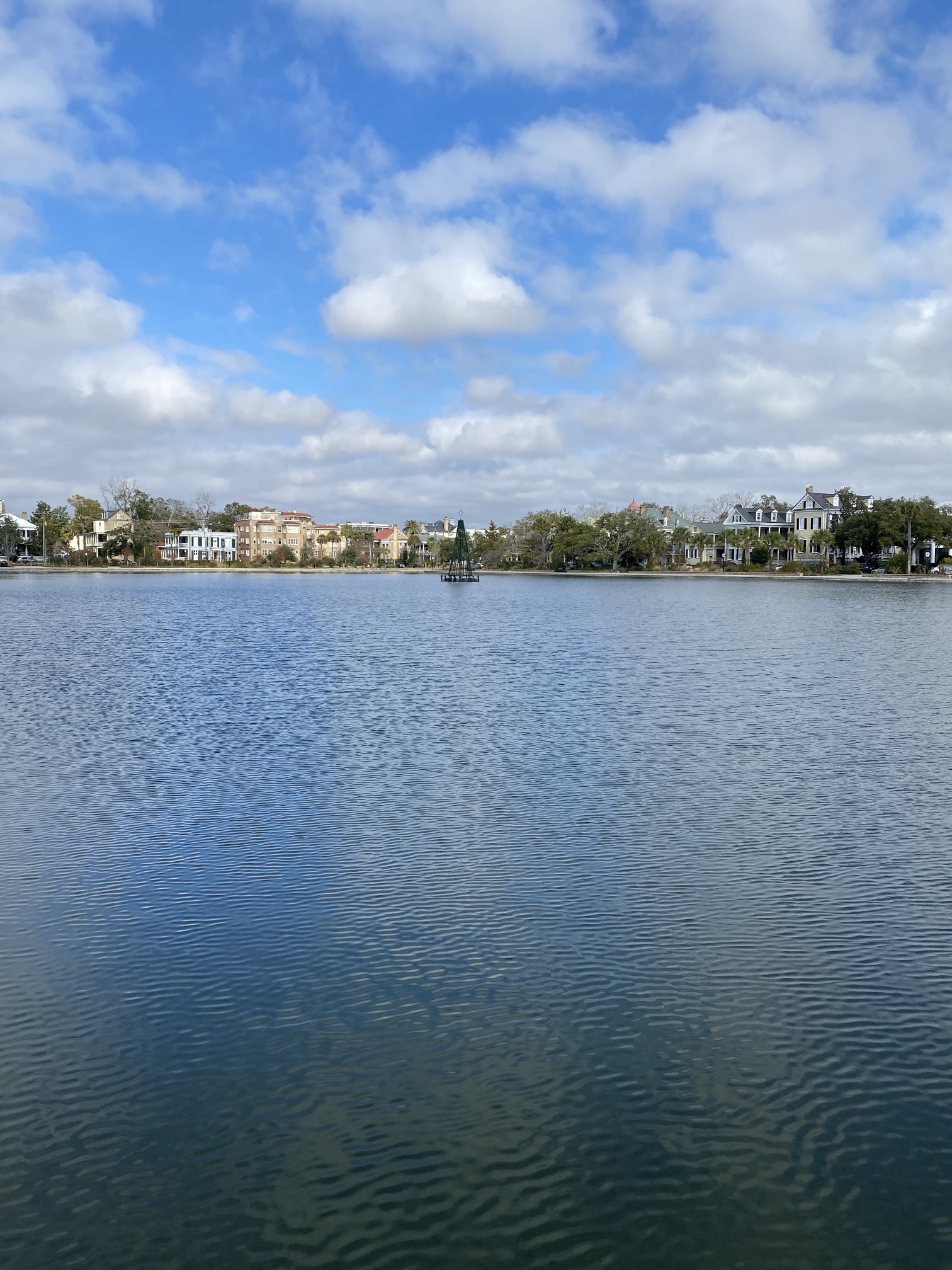 Colonial Lake under a cloudy blue sky, with houses along the far side and a Christmas tree frame in the water